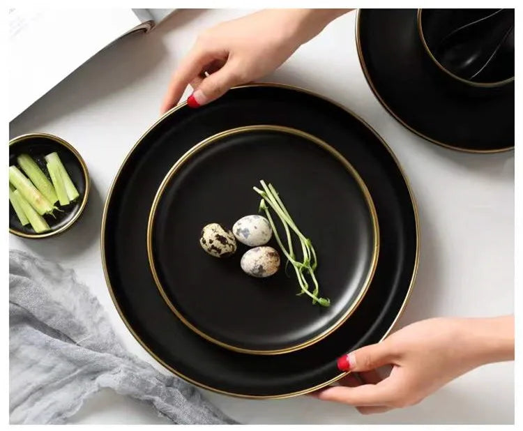 Set of black porcelain dinner plates and bowls with cutlery, featuring ceramic food dishes for rice, salad, and noodles.